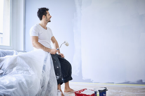 Lächelnder Mann sitzt in seiner neuen Wohnung und macht eine Pause vom Malen - BSZF00432