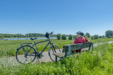 Germany, Zons, senior man with bicycle resting on a bench looking at view - FRF00658