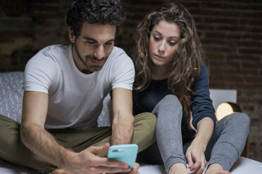 Couple sitting up on bed looking at smartphone - CUF06836