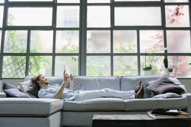 Man lying on sofa using digital tablet - CUF06849