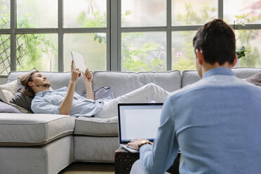 Männer entspannen sich auf dem Sofa und benutzen ein digitales Tablet und einen Laptop - CUF06857