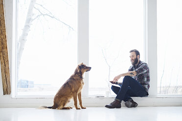 Young male designer with dog in design studio window seat - CUF06863