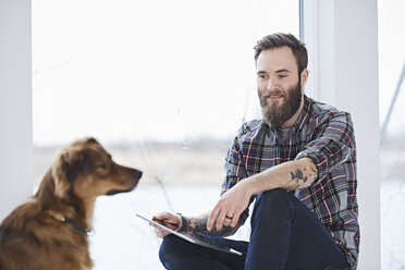Young male designer with dog in design studio window seat - CUF06864