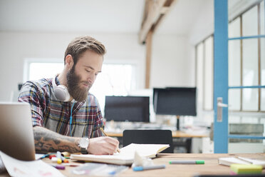 Junger männlicher Designer schreibt Notizen am Schreibtisch im Designstudio - CUF06883