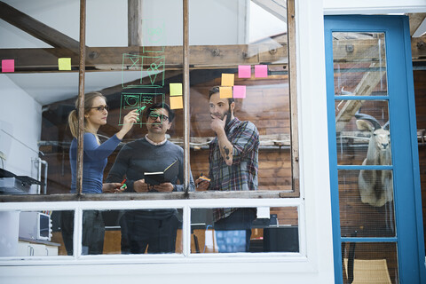 Designteam schreibt auf Haftnotizen und zeichnet am Fenster des Designstudios, lizenzfreies Stockfoto