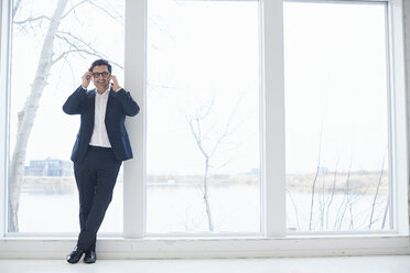 Male designer making smartphone call leaning on design studio window - CUF06913