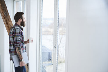 Junger männlicher Designer schaut durch ein Fenster im Designstudio - CUF06923