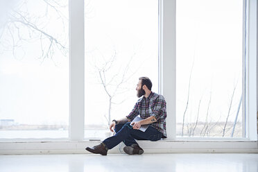 Junger männlicher Designer, der vom Fensterplatz eines Designstudios aus durch das Fenster schaut - CUF06924