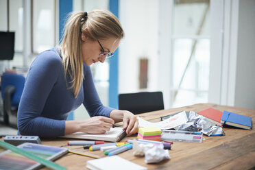 Female designer making notes at design studio desk - CUF06926