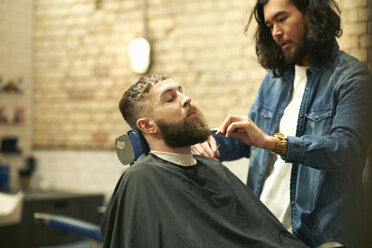 Friseurin im Friseursalon trimmt den Bart eines Kunden - CUF06971