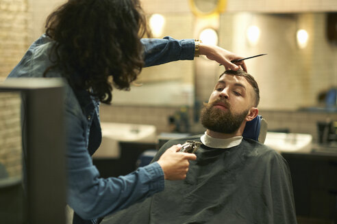 Friseurin im Friseursalon trimmt den Bart eines Kunden - CUF06972