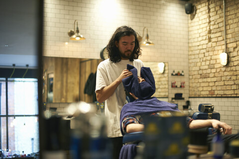 Friseurin im Friseursalon wickelt Kundin in Handtuch, lizenzfreies Stockfoto