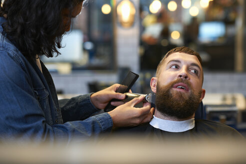 Friseurin im Friseursalon trimmt den Bart eines Kunden - CUF06983