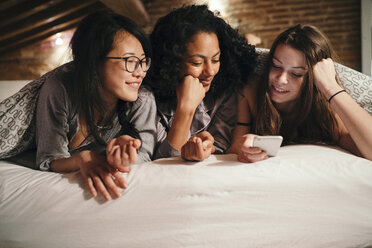 Friends lying on bed looking at smartphone - CUF06984