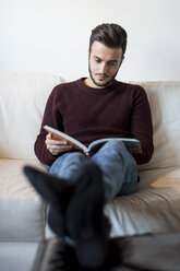 Junger Mann entspannt sich auf dem Sofa und liest ein Buch - CUF07004