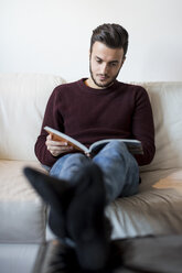 Young man relaxing on sofa, reading book - CUF07004