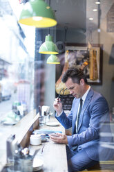 Reifer Geschäftsmann schaut auf Smartphone in Restaurant Fensterplatz - CUF07054