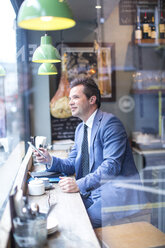 Mature businessman with smartphone in restaurant window seat - CUF07055