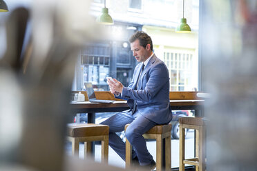Mature businessman looking at smartphone in restaurant - CUF07063