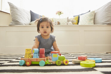 Portrait of baby girl sitting on rug playing with toy train - CUF07095