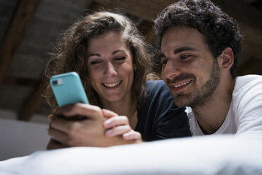 Young couple lying on bed looking at smartphone - CUF07139