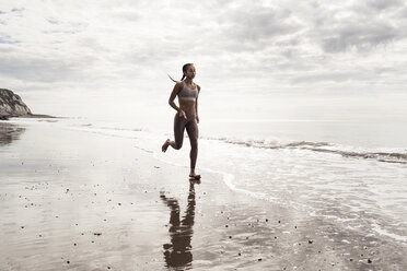 Young female runner running barefoot along water's edge at beach - CUF07151