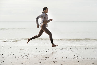 Seitenansicht einer jungen Läuferin, die barfuß am Strand entlang läuft - CUF07154