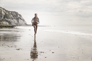 Vorderansicht einer jungen Läuferin, die barfuß am Strand entlang läuft - CUF07155