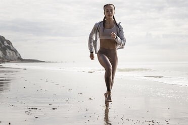 Front view of young female runner running barefoot along beach - CUF07156