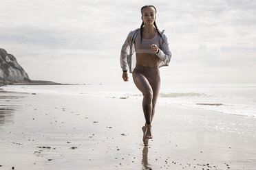 Vorderansicht einer jungen Läuferin, die barfuß am Strand entlang läuft - CUF07156
