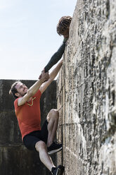 Young male free climber at top of sea wall helping friend climb up - CUF07159