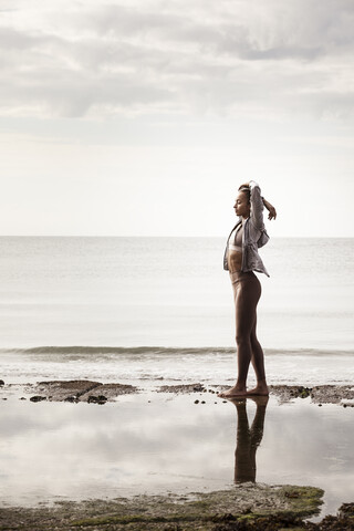 Junge Läuferin am Rande des Wassers am Strand und streckt die Arme, lizenzfreies Stockfoto