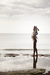 Junge Läuferin am Rande des Wassers am Strand und streckt die Arme - CUF07165