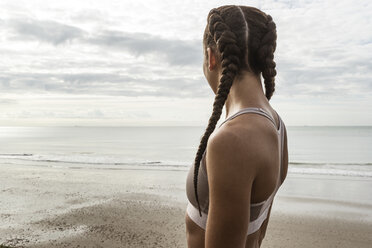 Junge Läuferin mit geflochtenen Haaren, die vom Strand aus auf das Meer schaut - CUF07167