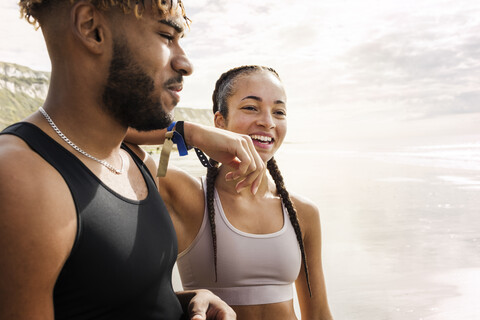Young female runner resting arm on young man's shoulder on beach stock photo