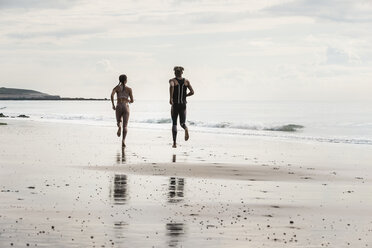 Rückansicht von jungen Läufern und Läuferinnen, die barfuß am Strand entlang laufen - CUF07173