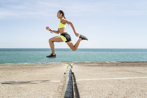 Junge Frau läuft im Freien, springt über eine Lücke in einer Brücke, mitten in der Luft, lizenzfreies Stockfoto