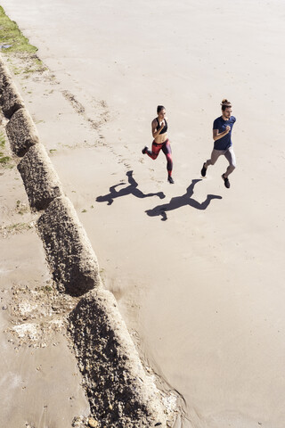 Junger Mann und Frau laufen am Strand entlang, Blick von oben, lizenzfreies Stockfoto