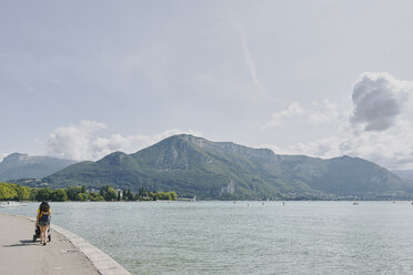 Rear view of woman strolling with pushchair waterfront at Lake Annecy, Annecy, Auvergne-Rhone-Alpes, France - CUF07279