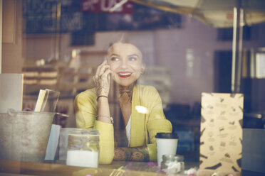 Junge Frau in einem Café sitzend, mit Smartphone, Tattoos auf der Hand, Blick durch das Fenster des Cafés - CUF07291