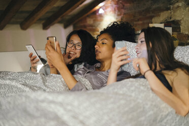 Freunde liegen nebeneinander im Bett und schauen auf ihre Handys - CUF07435