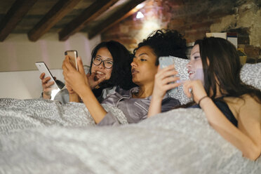 Friends lying side by side in bed looking at mobile phones - CUF07435