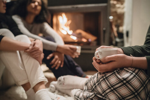 Friends in front of fire drinking coffee smiling - CUF07442