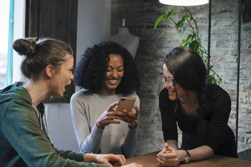 Freunde schauen lächelnd auf ihr Handy - CUF07443