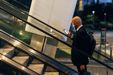 Reifer Geschäftsmann im Freien bei Nacht, auf Rolltreppe, mit Smartphone - CUF07479