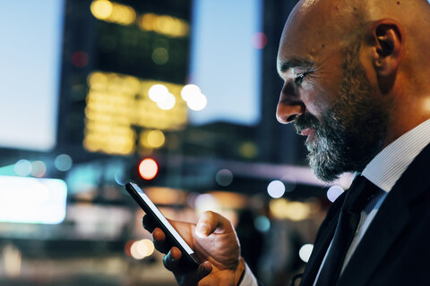 Erwachsener Geschäftsmann im Freien bei Nacht, der sein Smartphone benutzt, lizenzfreies Stockfoto