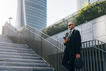 Älterer Geschäftsmann, der auf einer Treppe steht und ein Smartphone benutzt, niedriger Blickwinkel - CUF07481
