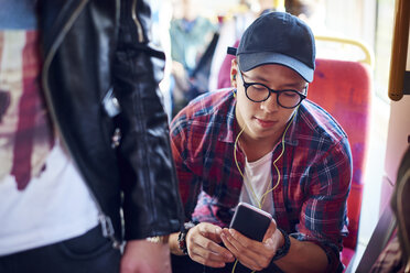 Junger Mann in der Straßenbahn, der auf sein Smartphone schaut und Kopfhörer hört - CUF07484