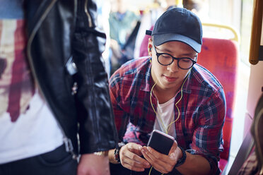 Young man on city tram looking at smartphone and listening to earphones - CUF07484