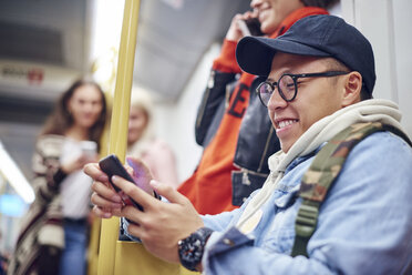 Junger Mann schaut in der Straßenbahn auf sein Smartphone - CUF07488